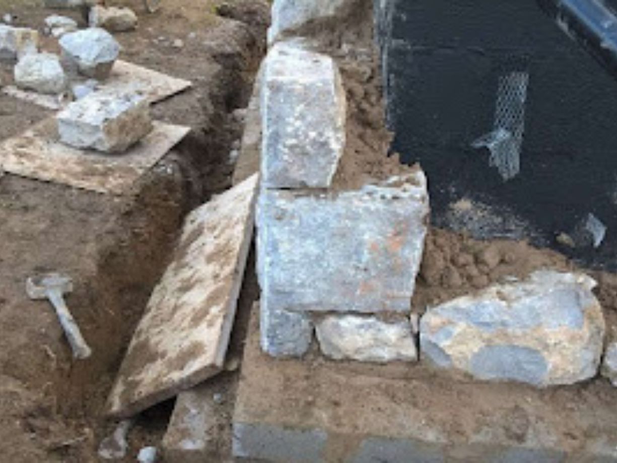 first layer of a stonewall with a newly dug trench and hammer on the ground