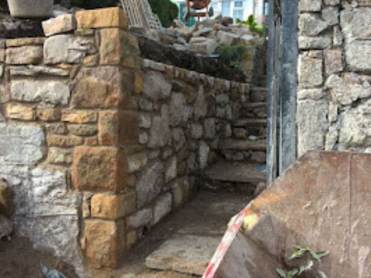 side view of a stone entrance with a black gate leading to a stone stairway