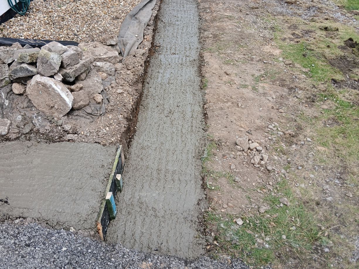 laying cement into a wall trench as the base foundaion for a cobbel stonewall